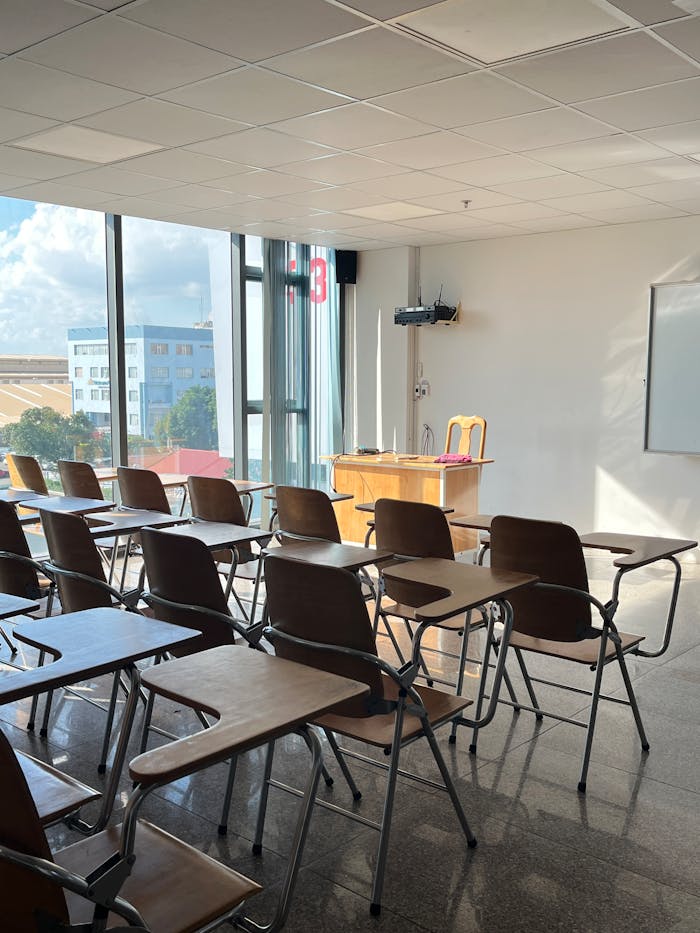 Bright, sunlit classroom with wooden desks and large windows offering a city view.